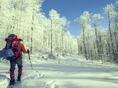 photo of winter backpacker hiking through a snowy path surrounded by trees